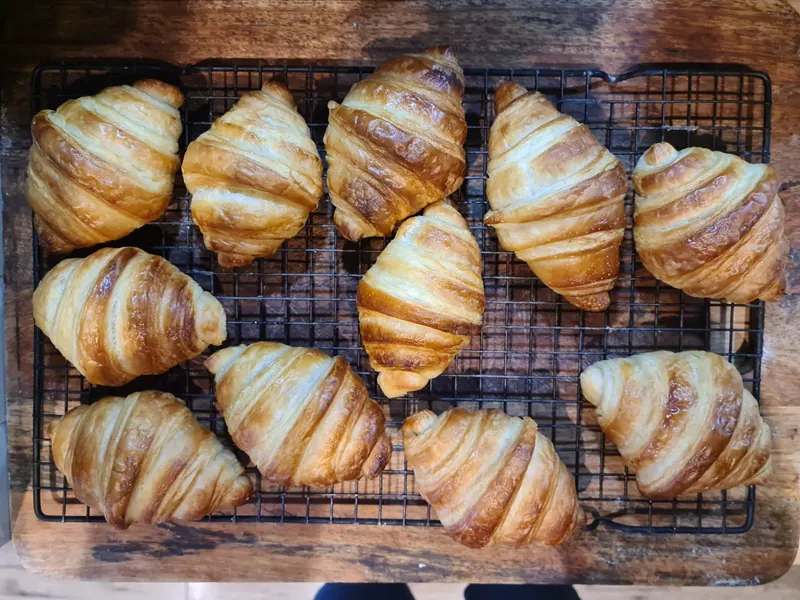 Golden croissants cooling on a wire rack on a wooden board