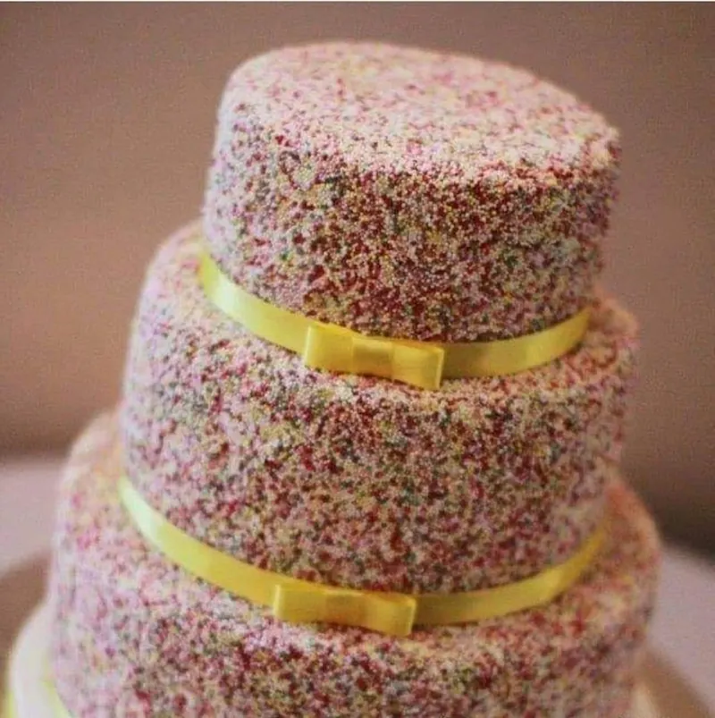 Three-tier cake covered in hundreds and thousands with yellow ribbon bows
