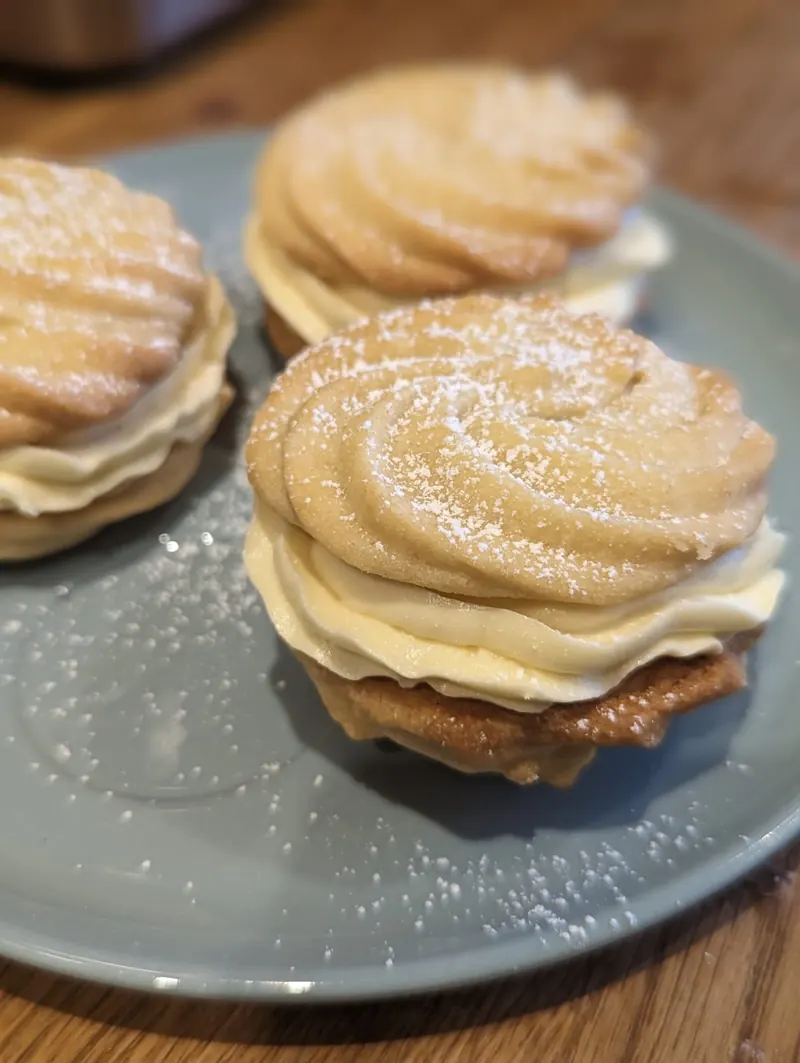 Viennese whirls sandwiched with piped vanilla buttercream and dusted with icing sugar, on a blue plate